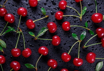  background of ripe wet cherries with water drops on a black background with green leaves close up top view © Pavlo