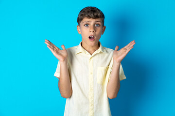 Surprised terrified Beautiful kid boy wearing casual shirt Gestures with uncertainty, stares at camera, puzzled as doesn't know answer on tricky question, People, body language, emotions concept