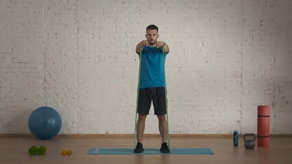 Man fitness coach in sportswear doing arms lifting exercise with rubber band for online class.