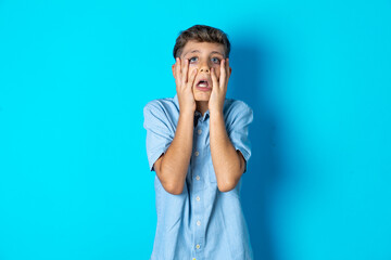 Sad lonely Beautiful kid boy wearing  casual blue shirt  touches cheek with hand bites lower lip and gazes with displeasure. Bad emotions