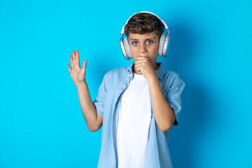 Happy Beautiful kid boy wearing  casual clothes sings favourite song keeps hand near mouth as if microphone wears wireless headphones, listens music