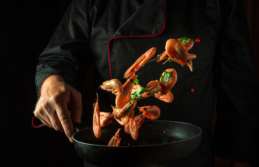The cook in his hand holds a frying pan with frozen shrimp and parsley. Isolated on black...