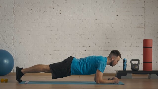 Closeup shot. Fitness coach in sportswear doing static low plank exercise at the home studio.