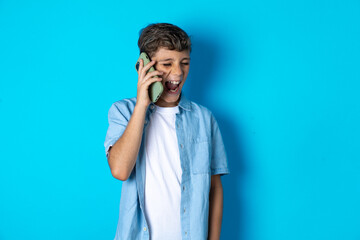 Overemotive happy Beautiful kid boy wearing  casual clothes laughs out positively hears funny story from friend during telephone conversation