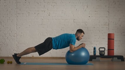 Closeup shot. Man fitness coach in sportswear doing elbow plank on fitball exercise.