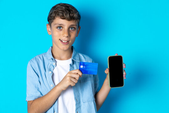 Photo of adorable Beautiful kid boy wearing  casual clothes holding credit card and Smartphone. Reserved for online purchases