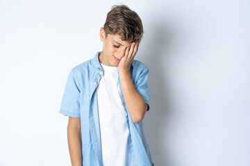 Tired overworked Beautiful kid boy wearing  casual clothes has sleepy expression, gloomy look, covers face with hand, has eyes shut, gasps from tiredness, fatigue after party