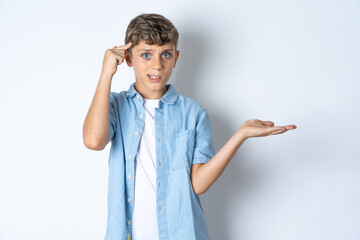 Fototapeta premium Beautiful kid boy wearing casual clothes confused and annoyed with open palm showing copy space and pointing finger to forehead. Think about it.