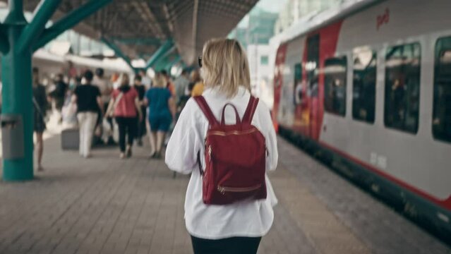A woman at the train station walks on a platform next to commuter trains. Daily use of public transport in urban life.