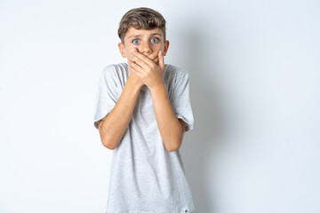Stunned Beautiful kid boy wearing grey casual t-shirt covers both hands on mouth, afraids of something astonishing
