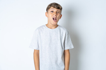 Beautiful kid boy wearing grey casual t-shirt yawns with opened mouth stands. Daily morning routine