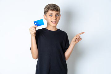 Smiling Beautiful kid boy wearing black casual t-shirt showing debit card pointing finger empty space