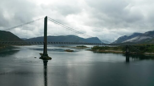 Kjerringstraumen suspension bridge spans above the Efjord. Mountains covered in fog tower on the horizon.