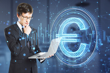 Attractive young european businessman using laptop with creative round euro coin and polygonal mesh hologram on blurry office interior background. Digital money and finance concept. Double exposure.