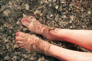 Women's legs in transparent water at the sea.