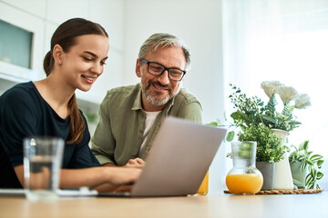 Portrait of a smiling mature father and young woman watching positive content on a laptop.