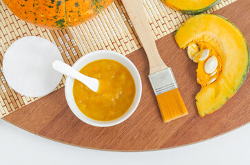 Homemade pumpkin face mask in a small white bowl and make-up brush. Natural autumn beauty treatment and spa recipe. Top view, copy space.