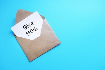On blue copy space background, envelope with note written GIVE 110% -  put absolute maximum amount of effort or energy possible - commitment to give it not less than 100 percent