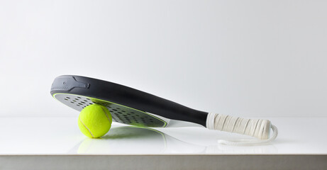 Black paddle tennis racket resting on a ball isolated white