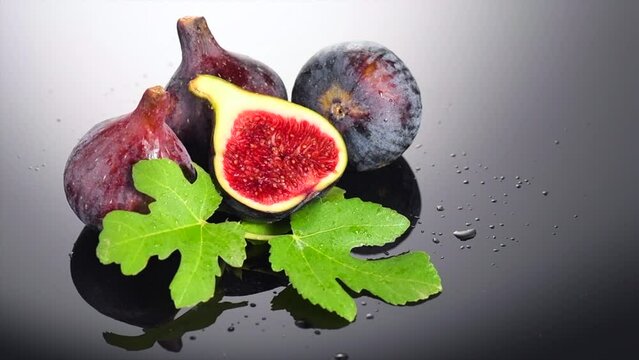 Fig fruits. Ripe sweet fresh figs fruit with leaves close up, on black background with water drops. Healthy sweet organic fruits
