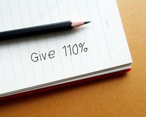 Pencil on notebook with handwritten text  GIVE 110% -  put absolute maximum amount of effort or energy possible - commitment to give it not less than 100 percent