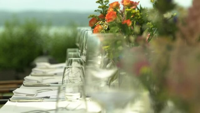 table arrangement with empty wine-glasses and flowers in natural garden colors and the focus shifting through the wine glasses towards the unfocused lake in the background