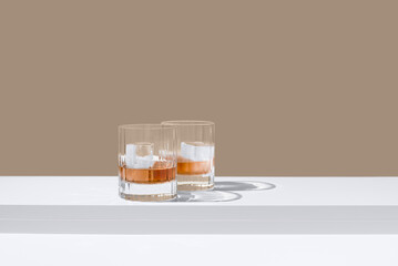 Dos vasos de whisky con hielo sobre un fondo marrón