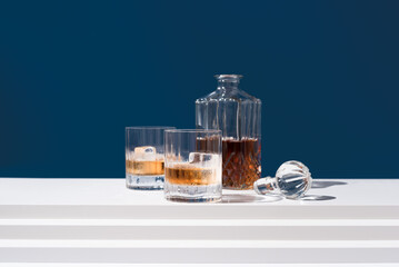 Dos vasos de whisky con hielo y decantador sobre fondo azul