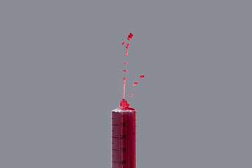 Jeringuilla vertiendo sangre sobre fondo gris