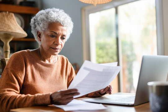 Senior Woman Retired Sit With A Laptop And Reading A Document. Pensive Older Woman With A Paper Bill Managing Her Finances, Planning Banking Loan Debt, And Paying Taxes Online Using A Computer. 