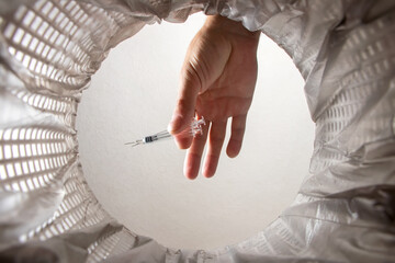 Hand throws syringe into trash bin with package. Inside view
