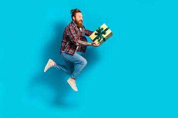 Full body photo of crazy man with beard dressed checkered shirt jeans run look in empty space hold gift isolated on blue color background