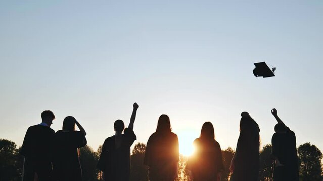 Silhouettes of Happy college graduates tossing their caps up at sunset.