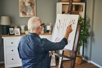 Elderly man painting on a canvas at home