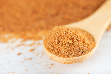 Unrefined cane sugar Panela in a wooden spoon on a white bacground, closeup, selective focus.