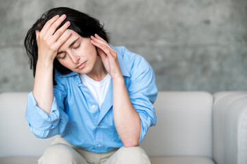 Portrait of tired woman holding forehead and suffering from headache