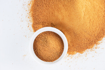 Bowl with heap of brown unrefined cane sugar Panela on white background, top view.