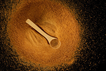 Pile unrefined cane brown sugar Panela with a wooden spoon on a black background, healthy food.
