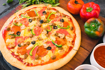 Supreme or Manhattan style pizza made with par-baked dough, using processed cheese. On a wood tray.