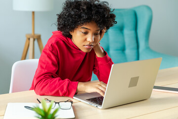 Obraz na płótnie Canvas African american girl using laptop at home office looking at screen typing chatting reading writing email. Young woman having virtual meeting online chat video call conference. Work learning from home