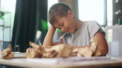 Portrait of exhausted school boy with failed crumped papers while writing in notebook at home Tired little kid child with creative block or lack of inspiration indoors Stress education concept