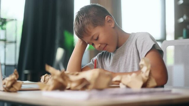 Portrait of exhausted school boy with failed crumped papers while writing in notebook at home Tired little kid child with creative block or lack of inspiration indoors Stress education concept