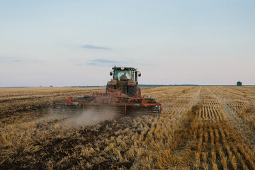 Fototapeta premium Modern tractor with a heavy trailed disc harrow works a wide hilly field. Autumn or spring agricultural campaign