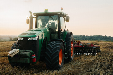 Close up photo of a modern green tractor with a red disc plow working with GPS for precision...