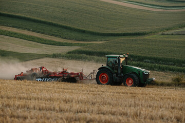 Fototapeta premium A tractor plows a wheat field. The concept of the work of a farmer and harvest.