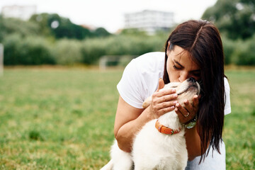 Kissing the animal. Woman with cute little golden retriever dog is on the green field