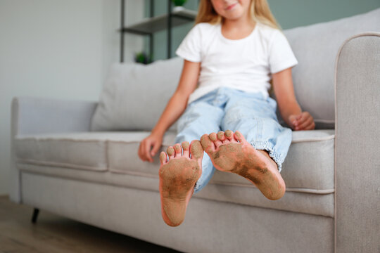 A child with dirty feet is sitting on the couch in the house. - Powered by Adobe