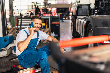 Confident mechanic sitting and talking on a smart phone in a workshop