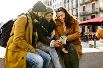 three happy friends using mobile phone on the street at winter. Group of students having fun outside