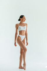 Against white background. Young woman with slim body type is in fitness clothes in the studio